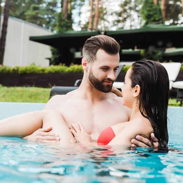 Selective focus of man looking at young woman smiling in swimming pool — Stock Photo