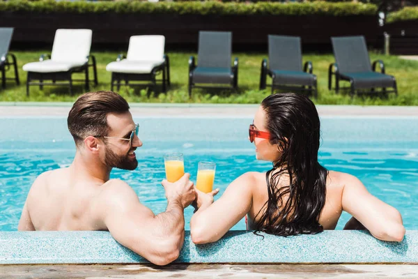 Bel homme barbu et belle femme dans des lunettes de soleil tenant des lunettes avec du jus d'orange — Photo de stock