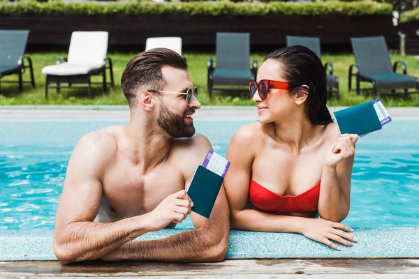 Feliz hombre y mujer en gafas de sol con pasaportes con billetes de avión - foto de stock