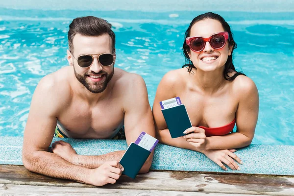 Homem alegre e mulher em óculos de sol segurando passaportes com passagens aéreas — Fotografia de Stock