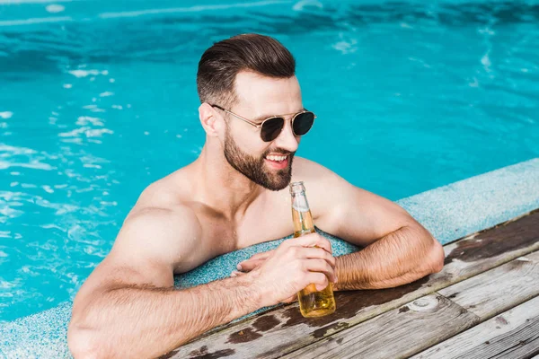 Hombre barbudo alegre en gafas de sol sosteniendo botella con cerveza - foto de stock
