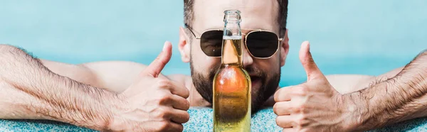 Panoramaaufnahme eines bärtigen Mannes mit Sonnenbrille, der Daumen hoch neben Flasche mit Bier zeigt — Stockfoto