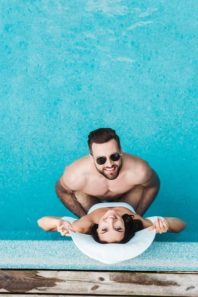 Вид зверху на щасливу жінку в солом'яному капелюсі і красивого чоловіка в сонцезахисних окулярах — стокове фото