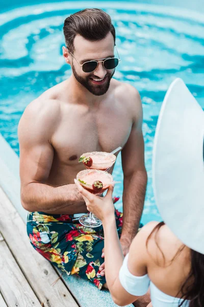 Enfoque selectivo de hombre feliz tintineo copas de cóctel con mujer en sombrero de paja — Stock Photo