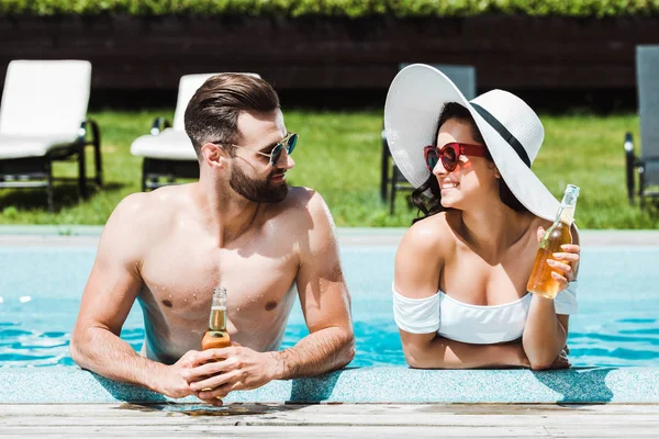 Mujer feliz en sombrero de paja sosteniendo botella con cerveza cerca de hombre guapo - foto de stock