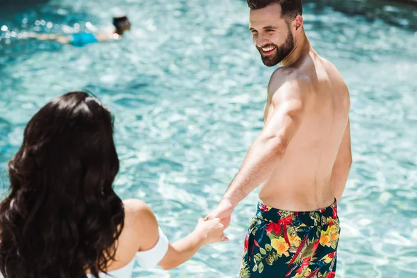 Selective focus of happy man and woman holding hands near swimming pool — Stock Photo