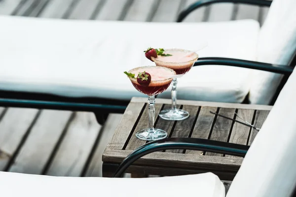 Foco seletivo de copos de coquetel com bebidas na mesa de madeira perto de cadeiras de praia — Fotografia de Stock