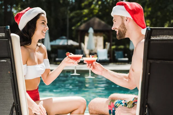 Feliz mulher e homem em sants claus chapéus clinking copos de cocktail — Fotografia de Stock