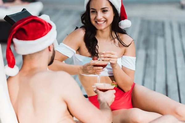 Vista trasera del hombre sosteniendo copa de cóctel cerca de mujer alegre en sombrero de Santa Claus - foto de stock