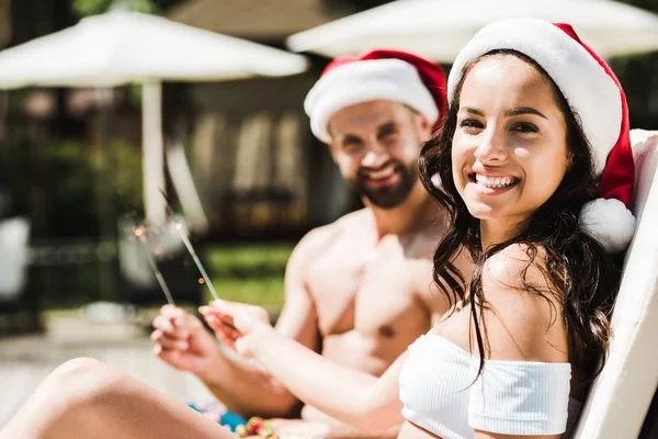 Enfoque selectivo de la mujer feliz en el sombrero de Santa Claus y el hombre sosteniendo chispas - foto de stock