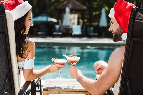 Donna allegra e uomo in pantaloni cappelli claus clinking bicchieri da cocktail — Foto stock