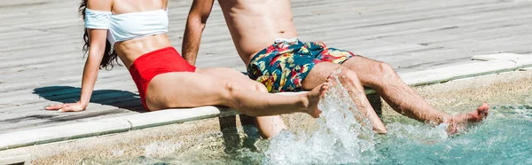 Panoramic shot of man and woman sitting on wooden decks near swimming pool — Stock Photo