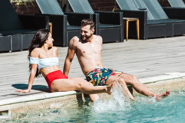 Happy man looking at woman while sitting on wooden decks near swimming pool — Stock Photo