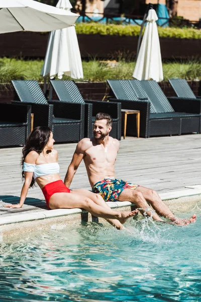Homem alegre olhando para a mulher enquanto sentado em decks de madeira perto da piscina — Fotografia de Stock