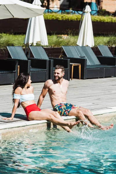 Cheerful man looking at woman while sitting on wooden decks near swimming pool — Stock Photo