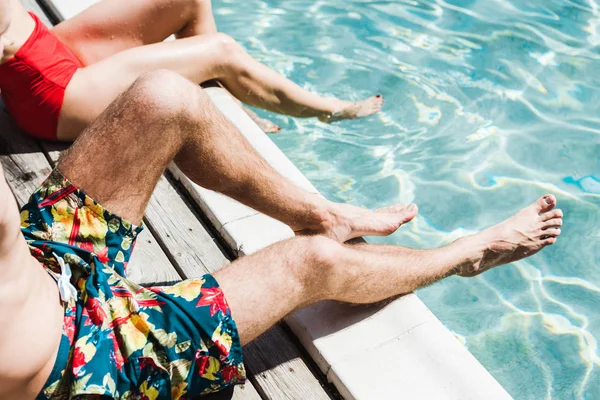 Vue recadrée de l'homme et de la femme assis sur des terrasses en bois près de la piscine — Photo de stock