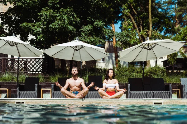 Beautiful woman and handsome man meditating near swimming pool — Stock Photo