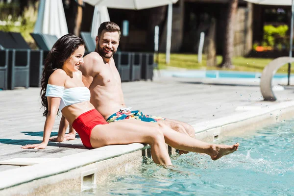 Homme et femme joyeux avec pieds nus assis sur des terrasses en bois près de la piscine — Photo de stock