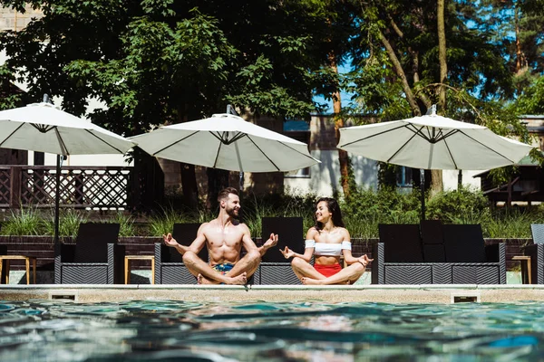 Selektiver Fokus einer glücklichen Frau und eines gutaussehenden Mannes, die in der Nähe eines Swimmingpools meditieren — Stockfoto