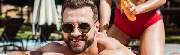 Panoramic shot of woman holding bottle with sunblock near happy man in sunglasses — Stock Photo