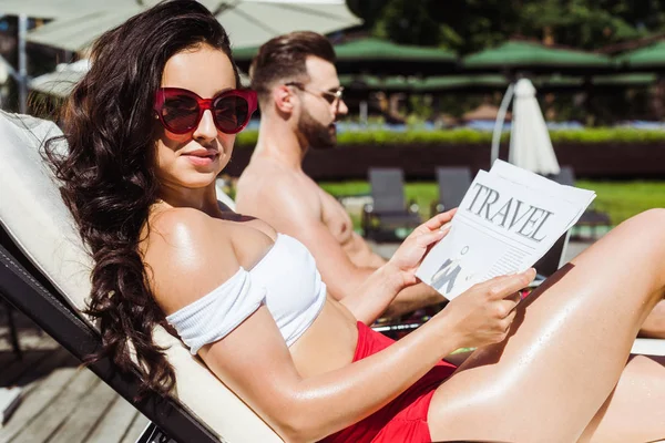 Selective focus of happy woman in sunglasses holding travel newspaper near man — Stock Photo