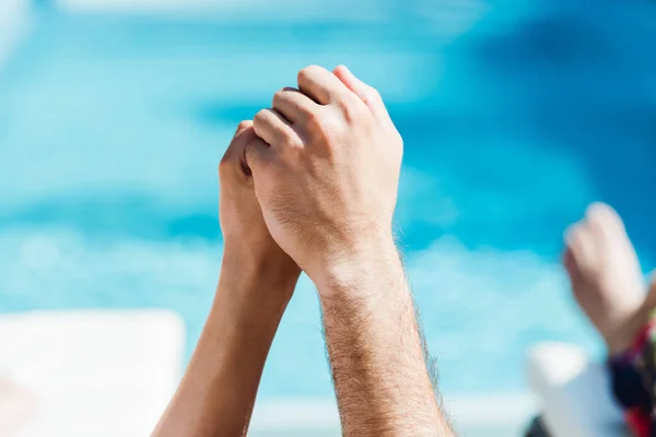 Vista recortada del hombre y la mujer tomados de la mano cerca de la piscina - foto de stock