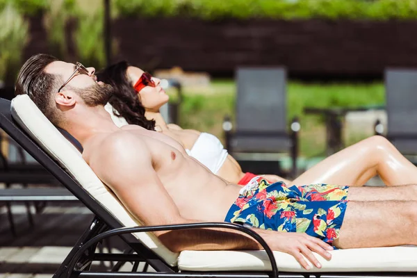 Enfoque selectivo del hombre muscular en gafas de sol tumbado en la silla de cubierta cerca de la mujer - foto de stock