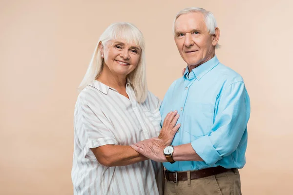 Fröhliches Seniorenpaar lächelt im Stehen auf beige — Stockfoto