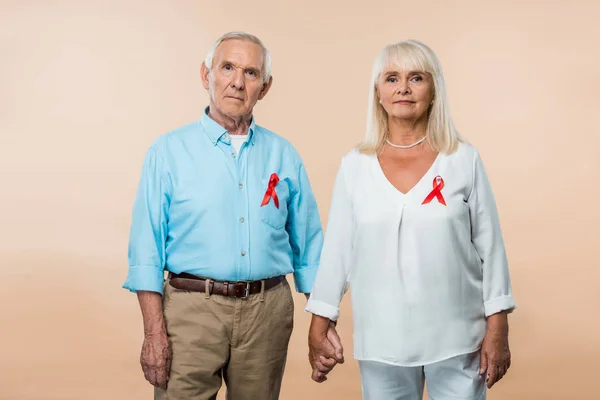 Senior couple with red ribbons as hiv awareness holding hands on beige — Stock Photo