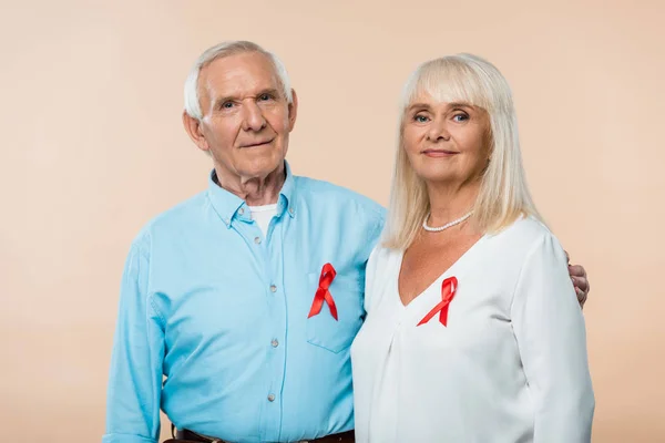 Happy senior couple with red ribbons as hiv awareness isolated on beige — Stock Photo