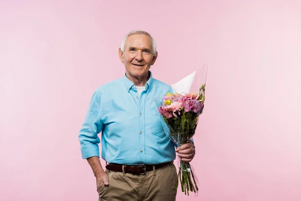 Fröhlicher älterer Herr, der mit der Hand in der Tasche steht und einen Strauß auf rosa hält — Stockfoto