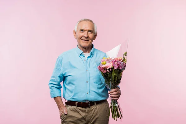 Alegre hombre mayor de pie con la mano en el bolsillo y la celebración de ramo de color rosa - foto de stock
