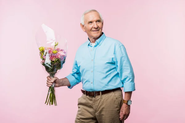 Cheerful senior man holding bouquet with flowers while standing on pink — Stock Photo