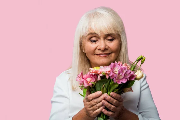 Щаслива старша жінка дивиться на букет квітучих квітів ізольовані на рожевому — стокове фото