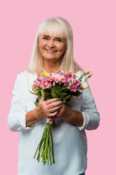 Glückliche Seniorin steht mit einem Strauß blühender Blumen auf rosa — Stockfoto