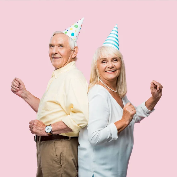 Positive senior husband and wife in party caps gesturing isolated on pink — Stock Photo