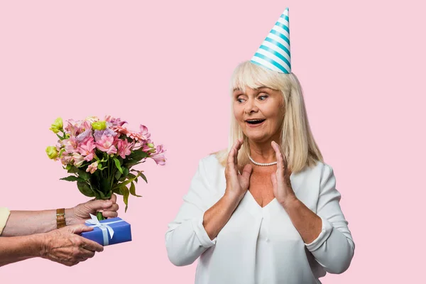 Cropped view of senior man giving presents to surprised wife in party cap isolated on pink — Stock Photo
