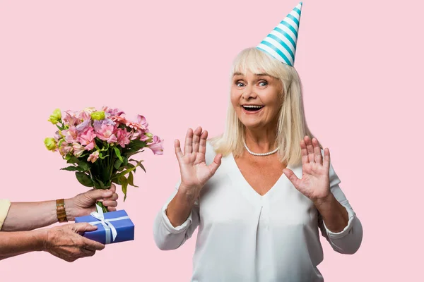 Abgeschnittene Ansicht eines älteren Mannes, der seiner glücklichen Frau in Partymütze Geschenke macht, isoliert auf rosa — Stockfoto