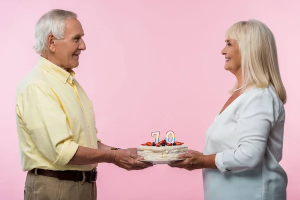 Heureux couple aîné avec cheveux gris tenant gâteau d'anniversaire isolé sur rose — Photo de stock