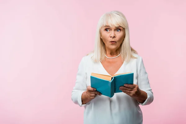 Überraschte Seniorin mit grauen Haaren hält Buch isoliert auf rosa — Stockfoto