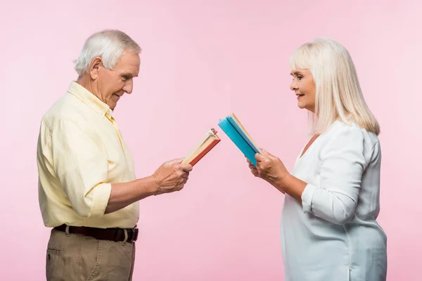 Vista laterale di felice coppia di anziani lettura libri mentre in piedi isolato su rosa — Foto stock