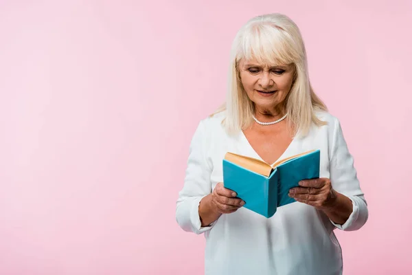 Donna anziana con capelli grigi libro di lettura isolato su rosa — Foto stock