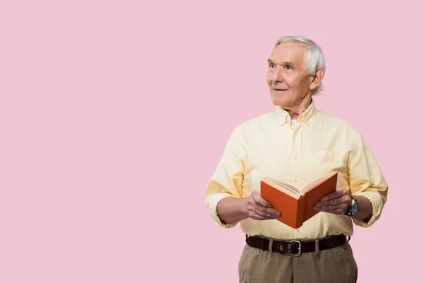Happy retired man holding book and smiling isolated on pink — Stock Photo