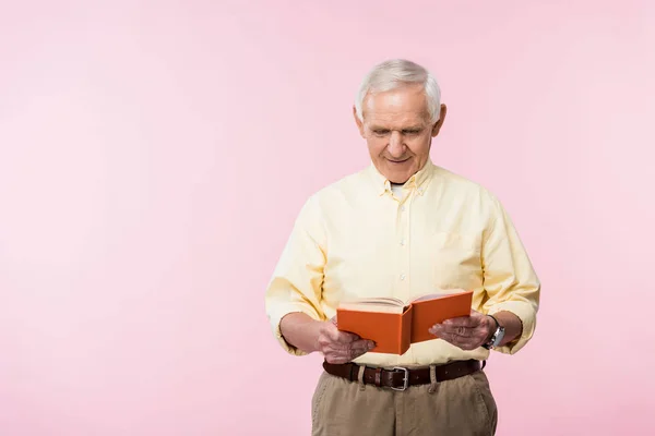 Hombre jubilado feliz leyendo libro y sonriendo en rosa - foto de stock