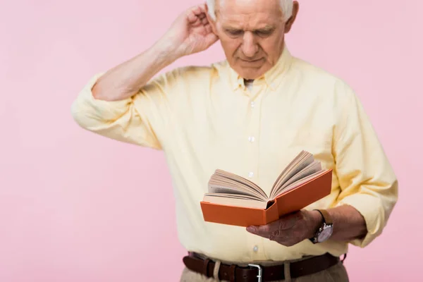 Thoughtful retired man reading book and touching grey hair on pink — Stock Photo
