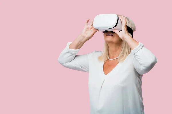 Женщина на пенсии в наушниках виртуальной реальности, изолированных на розовый — стоковое фото
