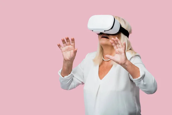 Женщина в отставке жесты в то время как носить гарнитуру виртуальной реальности изолированы на розовый — стоковое фото