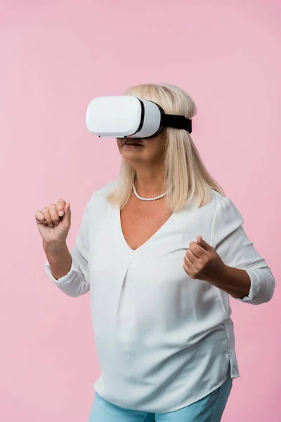 Senior woman wearing virtual reality headset and gesturing isolated on pink — Stock Photo