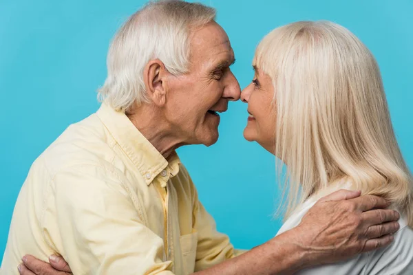 Homem aposentado feliz olhando para esposa alegre e sorrindo isolado no azul — Fotografia de Stock