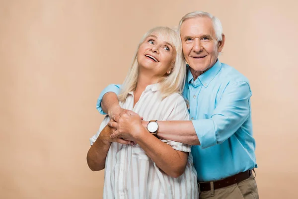 Happy pensioner hugging cheerful retired wife on beige — Stock Photo